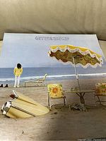 Front cover of Neil Young 'On The Beach' vinyl album showing beach scene with person, surfboards, umbrella, and chair.