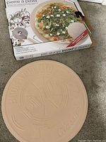 Pizza stone laid out with its original box showing the stone, metal pizza cutter, and metal stand.