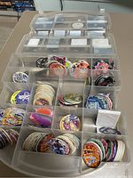 Top-view photo of the collection of pogs in a sectional plastic storage box. Multiple pogs with varied designs are visible, including popular franchises like Pokémon, Dragon Ball Z, and Yu-Gi-Oh.