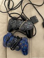 Two wired Sony PlayStation 2 controllers, one black and one translucent blue, coiled cables and button details visible.