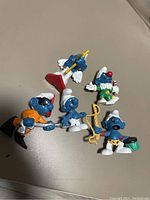 Five Smurf figurines with varied costumes and accessories on a beige background