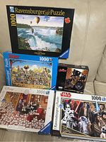 Photo showing five puzzle boxes including Ravensburger puzzles with Niagara Falls, whimsical character scene, Disney 101 Dalmatians, Star Wars puzzle, and one smaller Star Wars puzzle box.