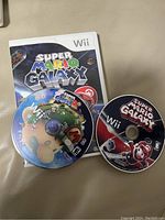 Two Wii game discs: Super Mario Galaxy with case and cover, plus Super Mario Galaxy 2 disc without case.