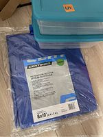 Blue polyethylene tarp in original packaging labeled Certified brand, size 8x10 feet, along with three clear plastic stackable storage containers with blue lids.