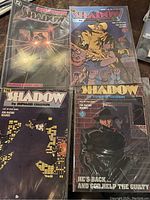 Four issues of The Shadow comic book series arranged together, showing front covers with dramatic artwork and title logos.
