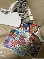 White Nintendo Wii console with two white Wii Remotes, two Nunchuk controllers, and five game cases placed on a beige surface.