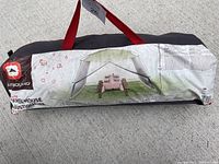 Packaged 12x12 Outbound Screen House tent in black bag with red handles, placed on concrete surface.