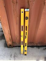 Two yellow 48-inch construction levels, one Stabila and one DeWalt, leaning against a rust-colored metal surface on concrete.