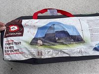 Photo of the black carrying bag with red handle showing the tent's branding and specifications including 8-person capacity and dome style.