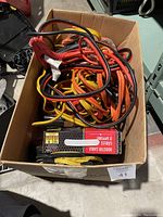 Box containing multiple pairs of booster cables, various colors and conditions, with one branded cable box visible.