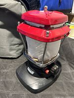 Coleman camping lantern with red top, protected glass globe, black base with power knob on a black surface.