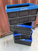 Four assembled collapsible plastic crates stacked, showing black sides and blue rims, one crate has CleverMade branding on rim.