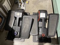 Pair of Cubii under desk elliptical machines showing textured foot pedals and body with control knobs.