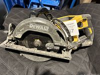 Side view of DeWalt cordless circular saw resting on a black surface, showing the blade guard and handle