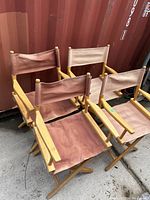 Four collapsible directors chairs arranged outdoors, showing wood frames and faded fabric seats and backrests.