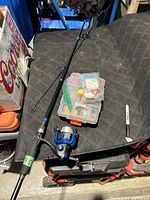 Full view of fishing rod assembled with spinning reel and tackle box on a black surface