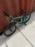 Side angle view of the green 20-inch Mongoose bicycle showing full frame, tires, seat, and handlebar with neon yellow brake cables.