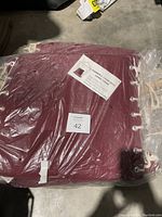 Photo showing burgundy hammock chair swing in packaging with label detailing size, materials, weight limit, and fade resistance.