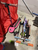 Four kids scooters arranged on concrete floor with red cover in background showing overall lot condition and color details