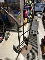 Front angle view of metal two-wheeled dolly with rubber grips on handles, welded frame bars, and flat platform with visible wear.