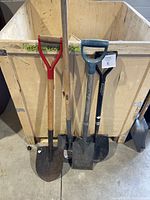 Four metal garden shovels with various handle styles and blade types leaning against a wooden crate