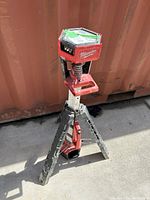 Milwaukee tripod tower light standing on a concrete floor next to a metal container wall, showing overall setup and condition.