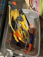 Top view of two Nerf bows in a plastic bin, showing a large yellow crossbow and a smaller bow along with several foam arrows.