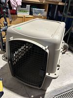 Front angled view of beige plastic pet cage with metal wire door and ventilation holes on sides.