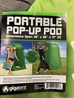 Tag showing product name, dimensions (36" x 36" x 7' height), usage context (beach, campers, photographers), and warnings. Green color pod illustrated on grass background.