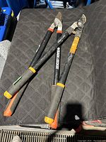 Two pairs of pruning shears on black quilted surface showing overall condition and size.