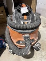 Front view of the orange and black Rigid shop vacuum with hose wrapped around it.