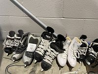 Photo showing seven pairs of skates lined up, including white figure skates and black hockey skates with visible size label 12 on one pair.