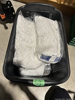 Five new white string mop heads inside a black plastic basket on the floor.