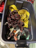 Plastic bin with yellow nylon tie straps and black/red edged tie straps with metal hooks.