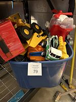 Blue tote filled with various toy trucks and a few large toy vehicles including a red fire helicopter toy.