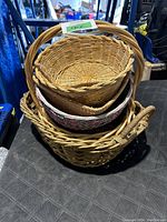 Stack of five wicker baskets of varying sizes and shapes, mainly oval with handles, one with a painted floral inner design.