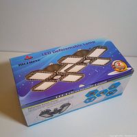 Blue and white retail box showing branding 'Morneve LED Deformable Lamp' and a visual of the 4-panel adjustable LED light, promotional text including 2 year warranty.