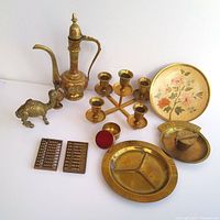 Full lot view showing all eight brass items including ewer, candle holders, camel figurine, abacuses, and ashtrays with plate.