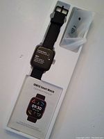 Smartwatch and manual in original packaging showing watch and instruction booklet.