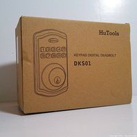 Box of HuTools keypad digital deadbolt lock, model DKS01, showing product sketch and brand on cardboard packaging.