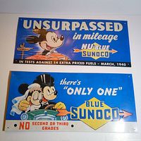 Two vintage Mickey Mouse Sunoco pressed metal sheet signs, one promoting Nu-Blue Sunoco mileage from 1940 with a signpost illustration, and the other showing Mickey and Minnie in a car advertising Blue Sunoco gasoline.