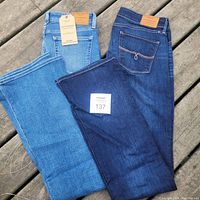 Two pairs of Lucky Brand women's jeans, one light wash new with tags, one dark wash used, laid flat on wooden surface.