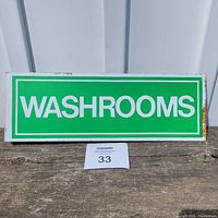 Front view of green and white 'WASHROOMS' sign, placed on wooden surface against white door.