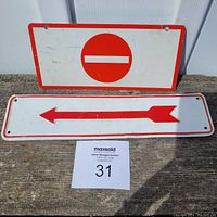 Photo of two metal road signs on concrete. One is a 'Do Not Enter' sign with a red circle and white bar. The other is a white sign with a red border and a left-pointing arrow.