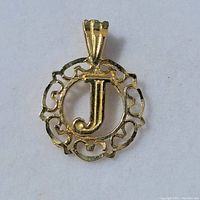 Front side of small circular pendant charm with intricate openwork border surrounding a raised letter J.