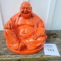 Front view of the orange resin Buddha statue seated on a circular base, showing overall condition and size relative to auction card.