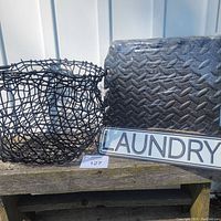 Photo showing the wire basket, laundry sign, and foam pads stacked together outdoors on wooden surface near vertical white panel siding.