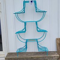 Front view of the turquoise wire plant stand showing pagoda shape and five shelves.