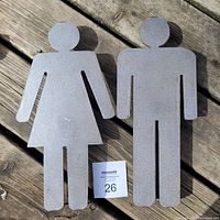 Front view of pair of steel washroom signs shaped as man and woman figures, matte gray finish