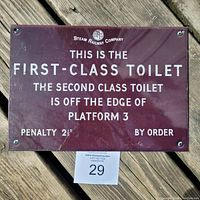 Full view of the UK Steam Railway Company metal sign with white text on a maroon background detailing directions for first and second class toilets with a penalty notice.